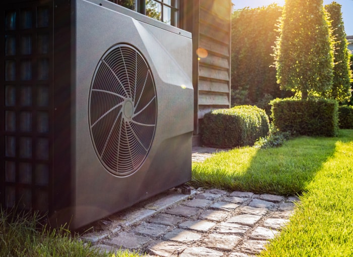 grande pompe à chaleur avec ventilateur à l'extérieur de la maison avec des arbres et des arbustes ensoleillés