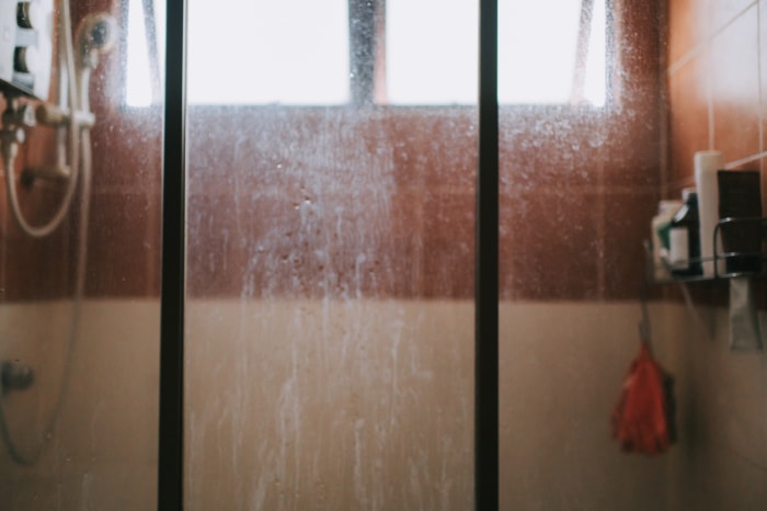 porte de douche devant la douche avec carrelage marron avec des traces de savon sur le verre