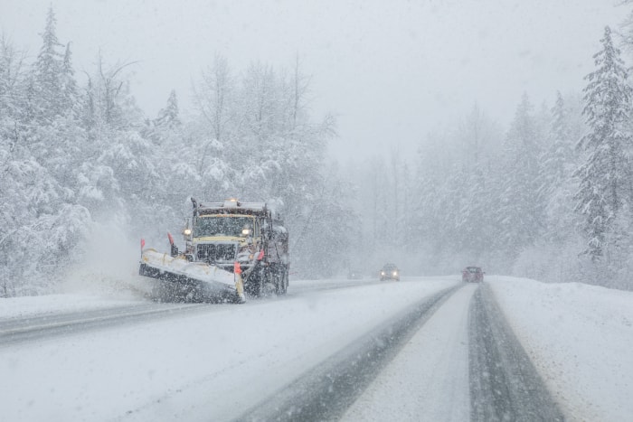 Camion de déneigement sur des routes enneigées à faible visibilité.