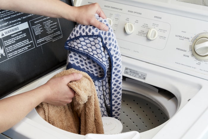 Une femme réorganise les serviettes dans une machine à laver à chargement par le haut.