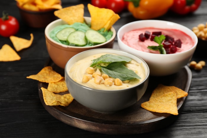 Différents types de houmous savoureux, de nachos et d'ingrédients sur une table en bois noir