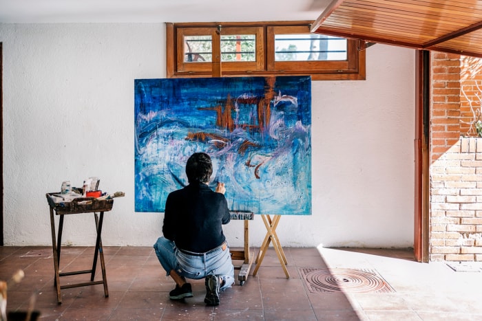 Femme peintre méconnue se relaxant dans son garage en train de peindre avec de la peinture bleue sur une grande toile.