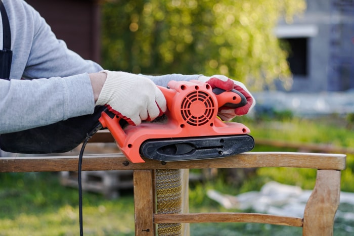 iStock-1340246837 comment utiliser une ponceuse à bande Gros plan d'un menuisier utilisant une ponceuse électrique pour restaurer un vieux stock de chaises