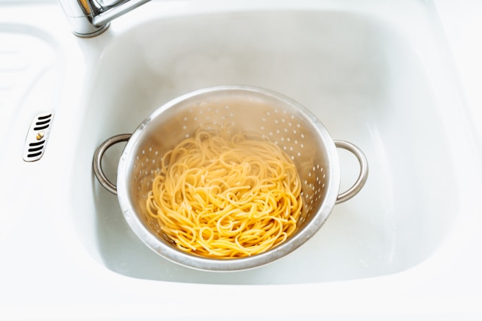 Faire bouillir les spaghettis dans une passoire blanche, à l'intérieur d'un évier de cuisine blanc.