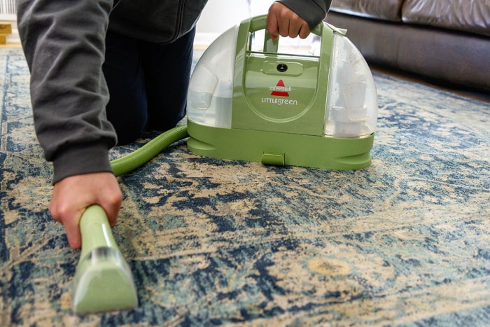 Une personne utilisant le meilleur nettoyeur de tapis portable pour nettoyer les taches sur un tapis à motifs.