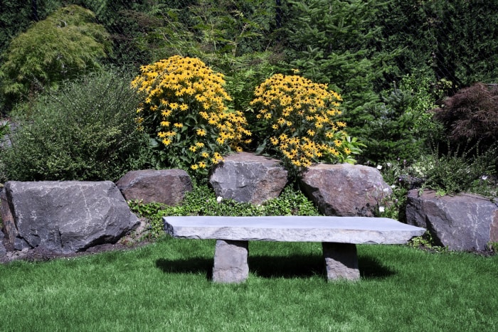 Banc de jardin en basalte assis dans une cour verte avec des fleurs jaunes.