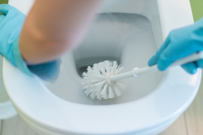 Mains gantées nettoyant la cuvette des toilettes à l'aide d'une brosse de toilette