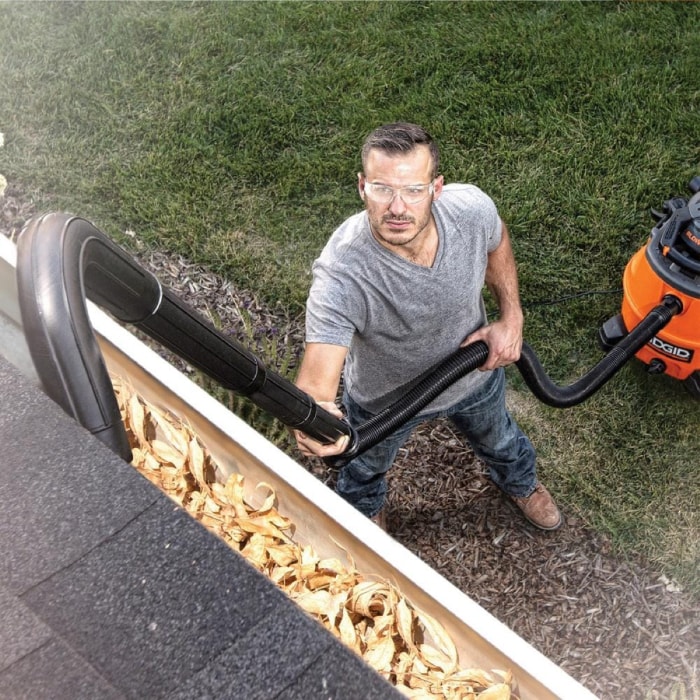 Un homme utilise un aspirateur pour nettoyer les gouttières.