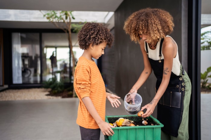 -parent-et-enfant-mettent-des-coquilles-d'œufs-dans-un-bac-à-compost-sur-une-terrasse.