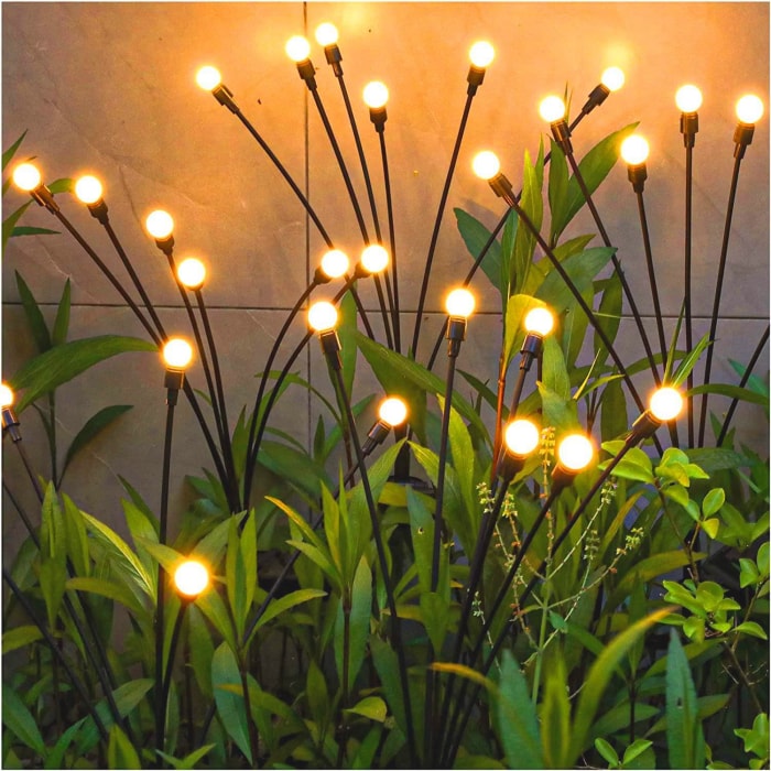 gros plan de petits piquets lumineux en forme de brins d'herbe parmi les plantes du jardin