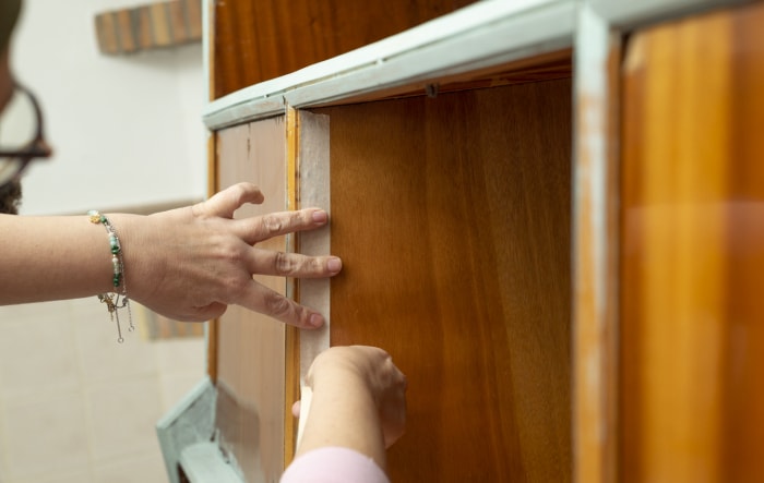 Une personne qui tapote une armoire en bois pour la teindre.