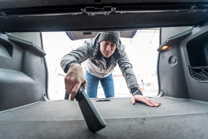 tâches d'entretien de voiture - homme utilisant un aspirateur dans le coffre de la voiture