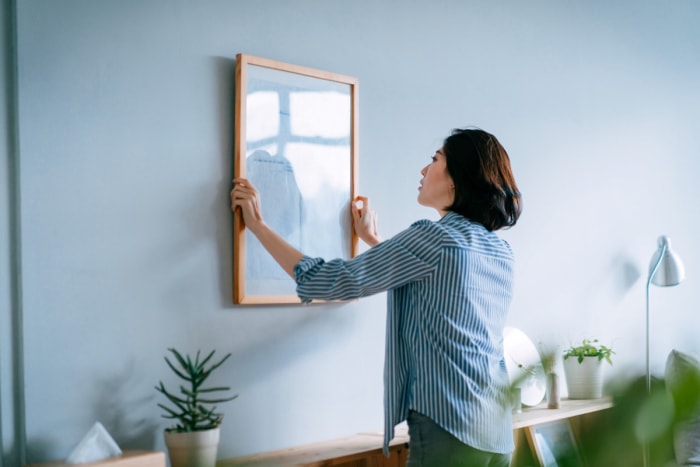 Femme accrochant un grand cadre photo sur un mur bleu.