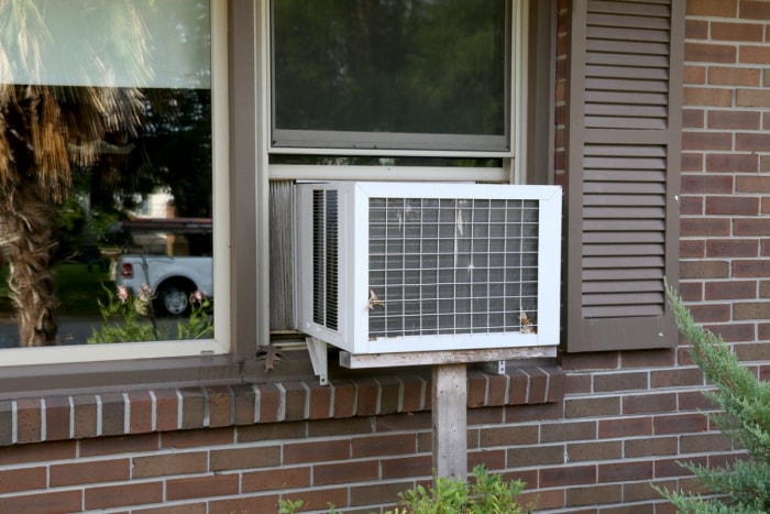 Un climatiseur est visible dans la fenêtre d'une maison en briques.