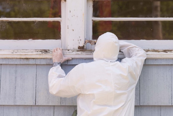 Professionnel en combinaison blanche en train d'enlever de la peinture à base de plomb.