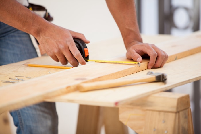 Gros plan d'un entrepreneur utilisant un mètre ruban pour marquer des dimensions sur une planche de bois