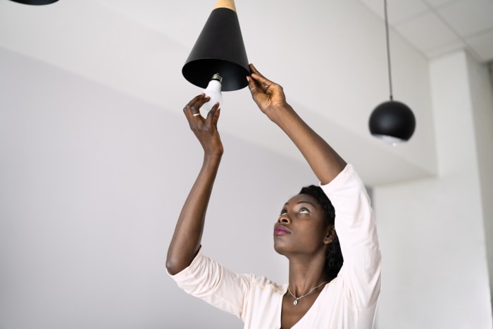 Une personne s'approche d'une lampe suspendue pour installer une ampoule LED.