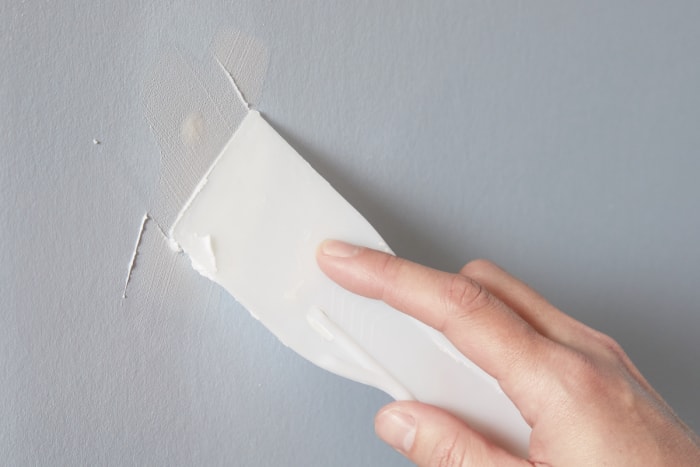 Une femme passe un couteau à mastic sur un trou dans une cloison sèche rempli de composé à joint.