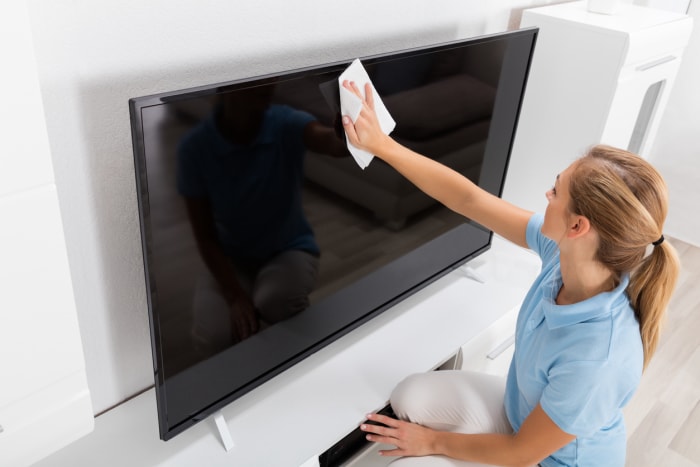 Jeune femme souriante essuyant la télévision dans le salon de sa maison