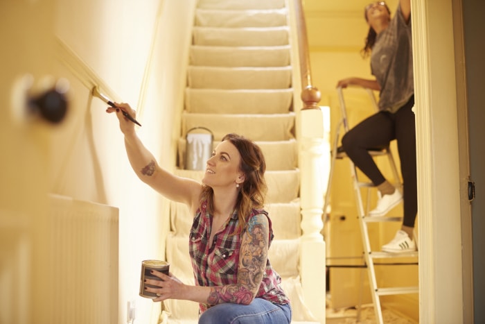 Une jeune femme tatouée peint un escalier avec l'aide d'une autre femme sur une échelle.