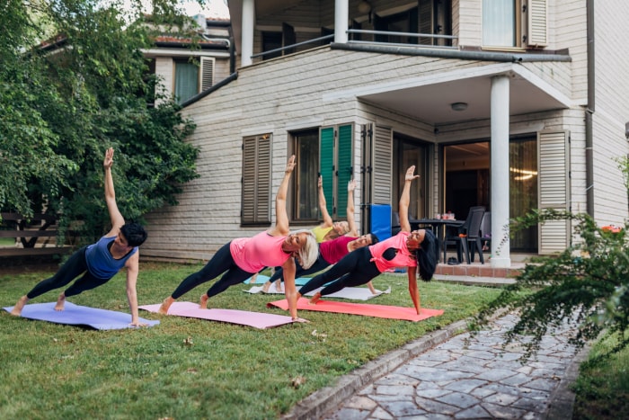 groupe de femmes en tenue de fitness faisant du yoga devant une maison de banlieue