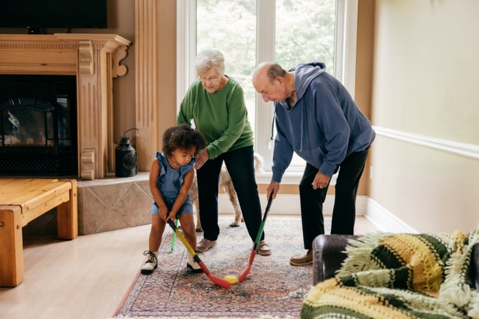 couple de seniors jouant au hockey avec leur petit-enfant sur un tapis persan dans le salon