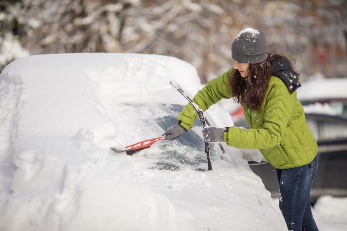 Une femme d'âge mûr nettoie sa voiture de la neige sur le parking. Elle porte des vêtements chauds et utilise une brosse à neige