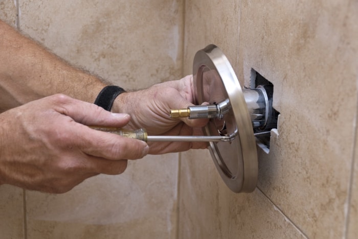 Une personne installant un robinet de douche et de baignoire de remplacement avec des compétences de plomberie de bricolage.