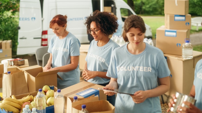 trois-femmes-bénévoles-tshirts-emballent-de-la-nourriture-dans-des-boîtes-en-carton-au-devant-d'un-van-de-livraison