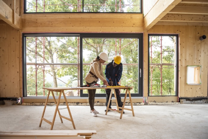 Un homme et une femme entrepreneurs portant des casques de sécurité dans la construction d'une nouvelle maison tout en examinant les plans.