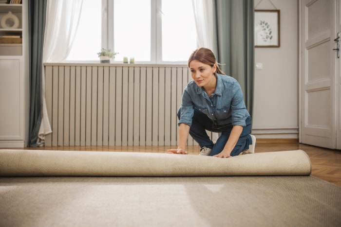 Une femme déroule un tapis sur son parquet.