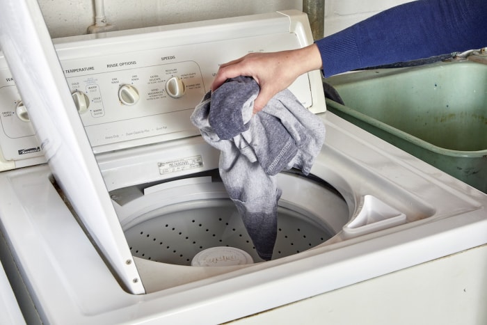 Une femme met une chemise dans une machine à laver à chargement par le haut.