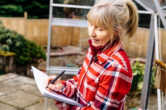 Une femme planifie avec un bloc-notes et un stylo dans son jardin.