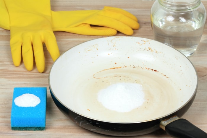 Poêle brûlée avec du bicarbonate de soude à côté d'un verre de vinaigre et de gants.