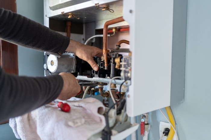 Une personne utilise des outils à l'intérieur d'un chauffe-eau sans réservoir ouvert.