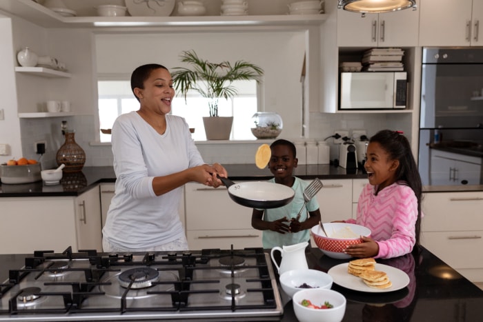 Vue de face d'une mère afro-américaine et de ses enfants préparant des aliments sur un plan de travail dans une cuisine à la maison