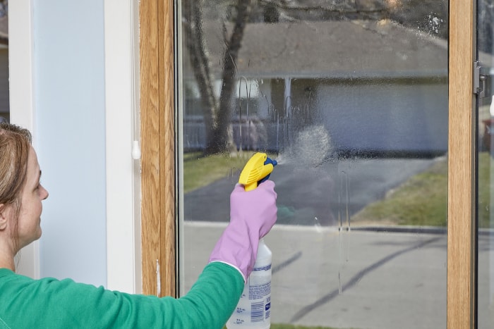 Une femme pulvérise une vitre intérieure avant de la nettoyer.