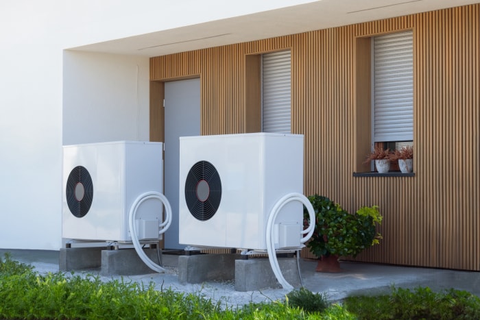 Deux pompes à chaleur électriques blanches branchées à l'extérieur et devant une maison moderne.