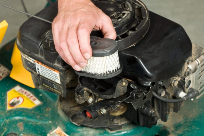 Une personne place un filtre à air propre à l’intérieur d’une tondeuse à gazon.