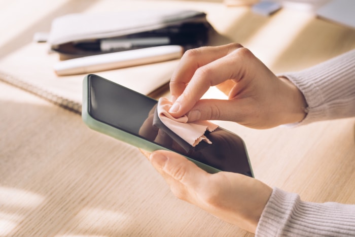 Gros plan d'une femme méconnaissable nettoyant la surface de son smartphone dans son bureau à domicile.