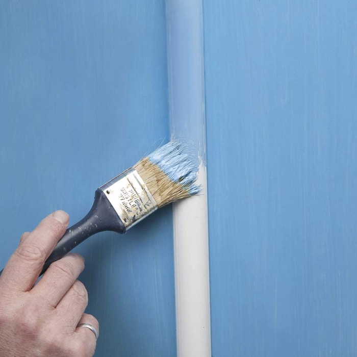 Une personne peint un chemin de câbles blanc en bleu clair pour l'assortir à la peinture murale bleu clair.