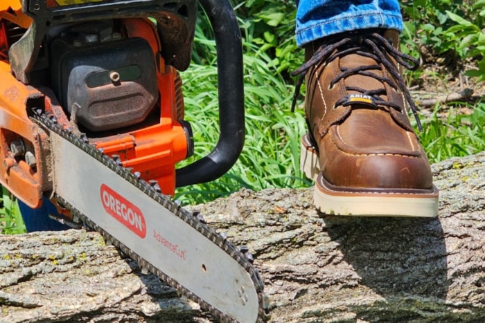 Personne marchant sur une bûche avec des bottes de travail Ariat Rebar Lift marron et une tronçonneuse.