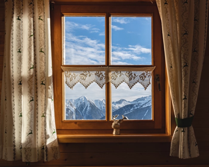 Rideaux blancs à motifs de cerfs verts sur une fenêtre avec vue sur la montagne