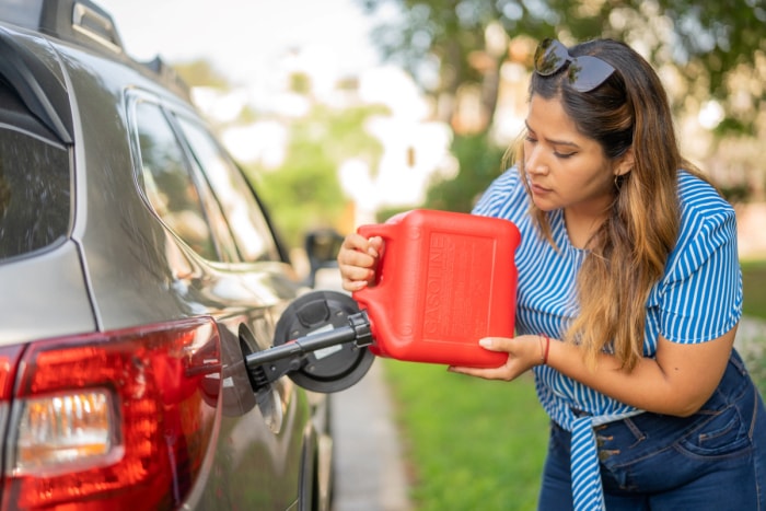 Une femme verse de l'essence d'un bidon rouge dans une voiture.