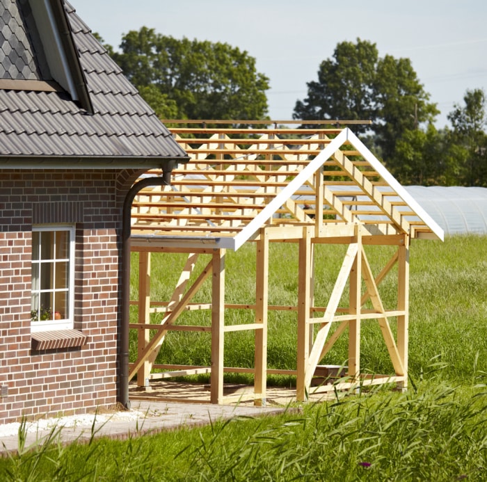 prise de vue extérieure au soleil. une partie d'une construction à ossature bois. à l'extérieur au soleil. gros plan d'une partie d'une maison familiale. paysage verdoyant en arrière-plan. Sur le côté droit, vous pouvez voir un nouvel échafaudage en bois. voici un endroit en pleine croissance