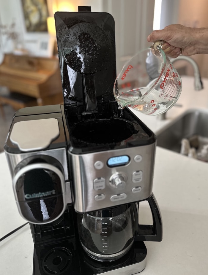 Un homme verse de l'eau et du vinaigre dans le réservoir d'une cafetière