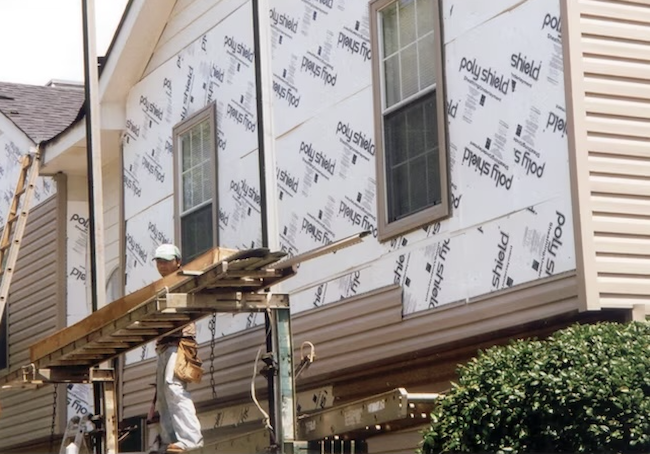 Panneau isolant en mousse rigide blanche sur le revêtement extérieur d'une maison avec des ouvriers du bâtiment.