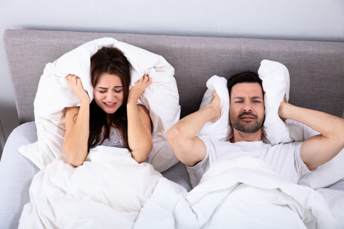 Couple perturbé se couvrant les oreilles avec un oreiller sur le lit