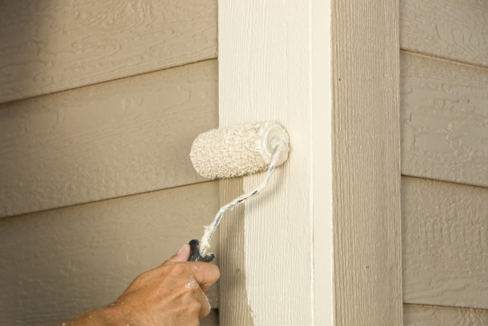 vue rapprochée du revêtement de la maison avec un rouleau à peinture peignant de la peinture blanche sur le revêtement