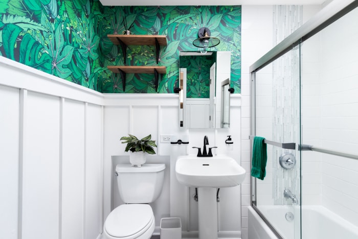 Une petite salle de bains est décorée de panneaux blancs et de lattes surmontés d'un papier peint botanique vert orangé.